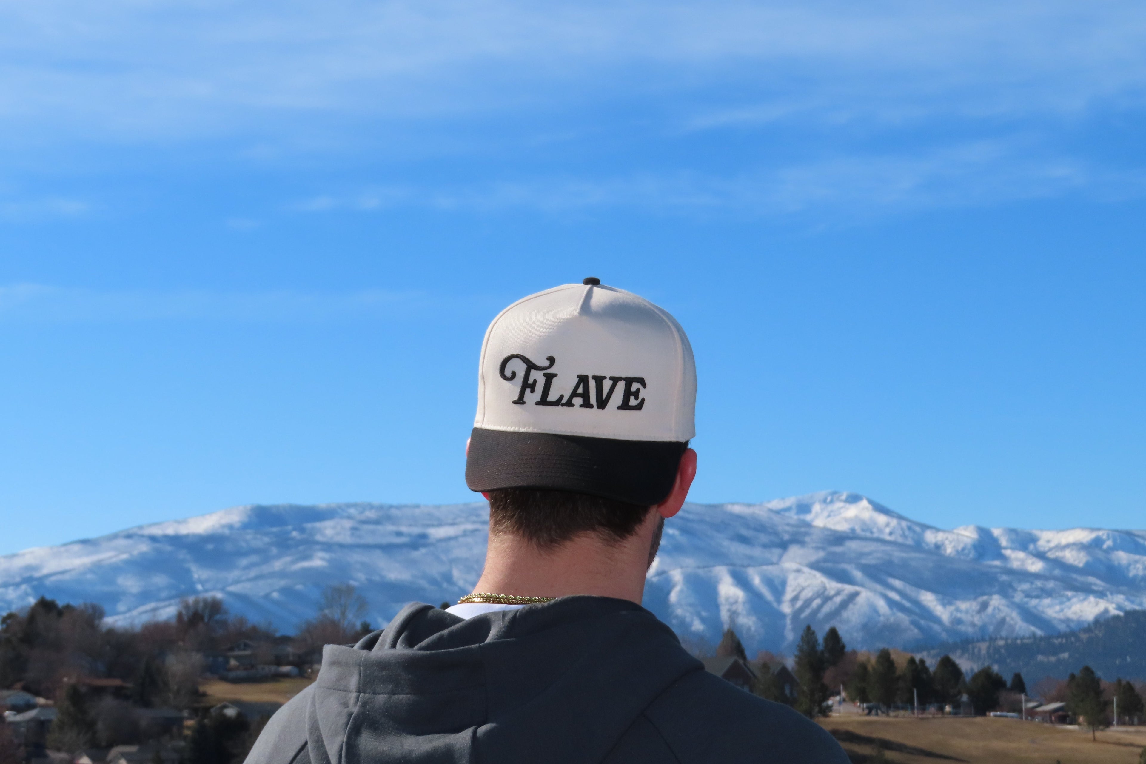 Person wearing a cap with 'FLAVE' logo, looking at snow-capped mountains